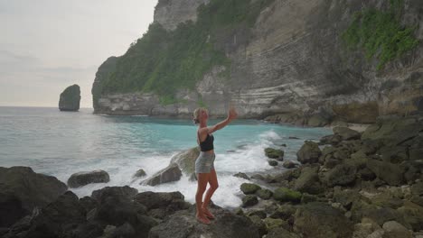 happy blond travel girl taking selfie on tembeling beach with tall cliffs