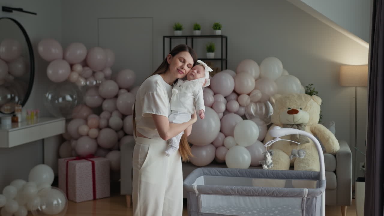 Mãe abraça carinhosamente seu bebê recém-nascido em um quarto decorado com balões e um ursinho de pelúcia