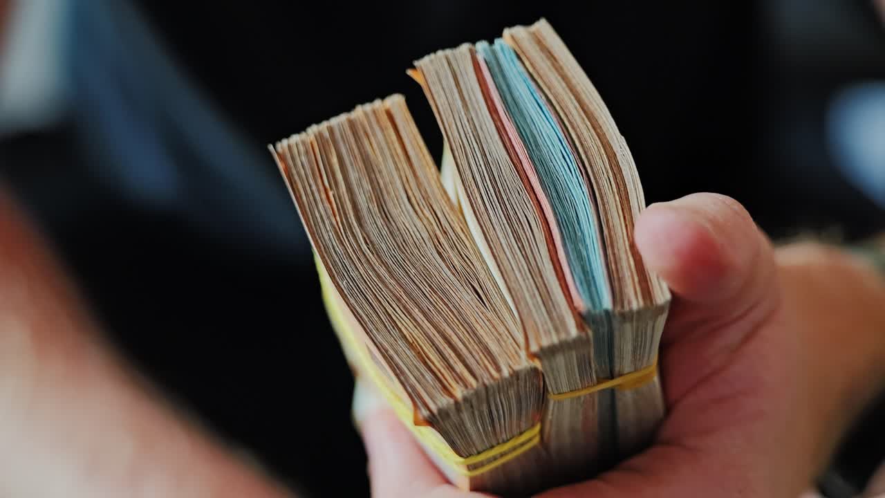 Rubber-banded euro bills tightly held in male hand with watch in daylight glow
