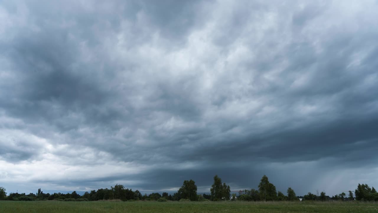 A storm is brewing over a natural landscape in a field. Rain clouds are forming and it begins to rain. A gloomy mood prevails in Switzerland. The wind is blowing the trees and grasses