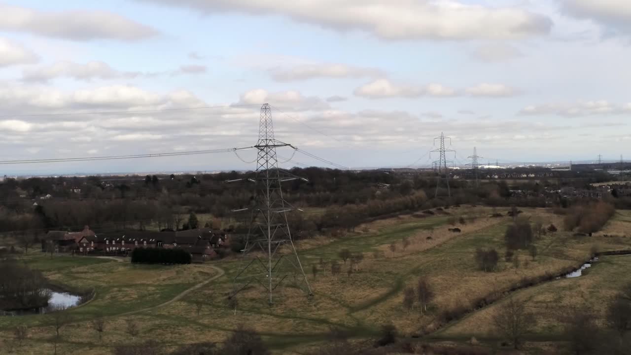 Flying Electricity distribution power pylon overlooking British parkland countryside, wide rising shot