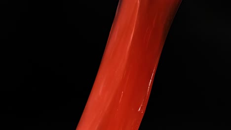 close-up of hands manipulating and stretching vibrant red slime against a dark background.