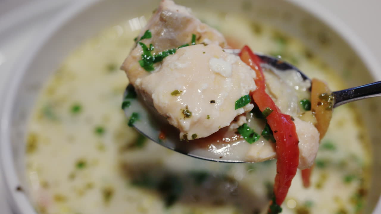 Primer plano de sopa cremosa de salmón con hierbas y verduras siendo removida con una cuchara
