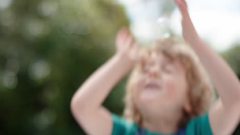 un niño lindo atrapando juguetón burbujas de jabón flotando con un niño feliz divirtiéndose haciendo estallar burbujas en un parque soleado juego de la infancia despreocupado 4k