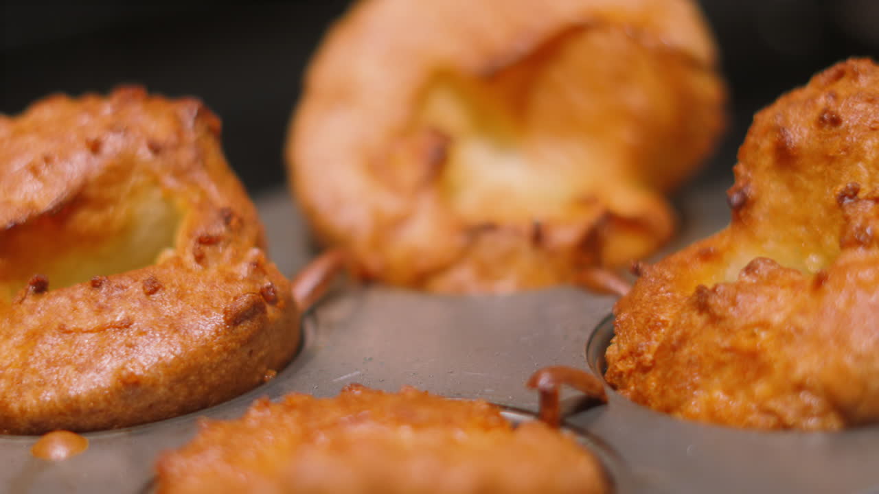 Vista a mano su vassoio di Yorkshire Puddings britannici appena cucinati con una consistenza dorata e croccante. Perfetto per spot pubblicitari alimentari di alta gamma, promozioni di arrosti della domenica britannici e intestazioni di ricette da far venire l'acquolina in bocca