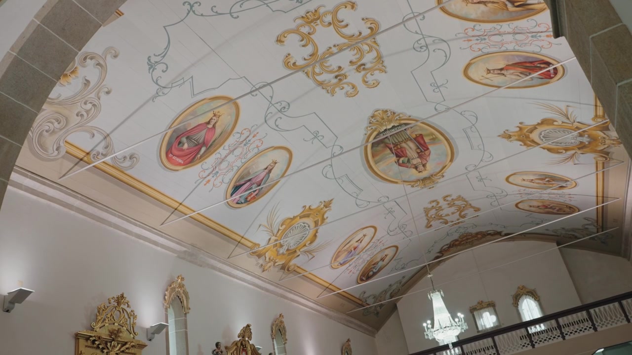 Soffitto ornato di chiesa con medaglioni di santi dipinti, volute dorate e lampadario