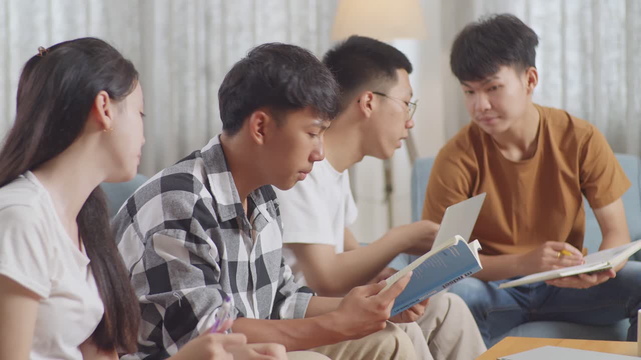 집에서 공부하는 아시안 십대 그룹의 클로즈업: 여자와 친구를 가르치는 책과 함께 플레이드 셔츠를 입은 소년, 노트북에 글을 쓰고 친구들과 논의하는 노트북을 들고 있는 소년.