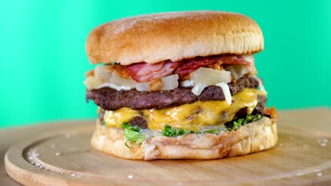 beef burger with cheese, sauce and vegetables rotating on a wooden board in front of green screen background.