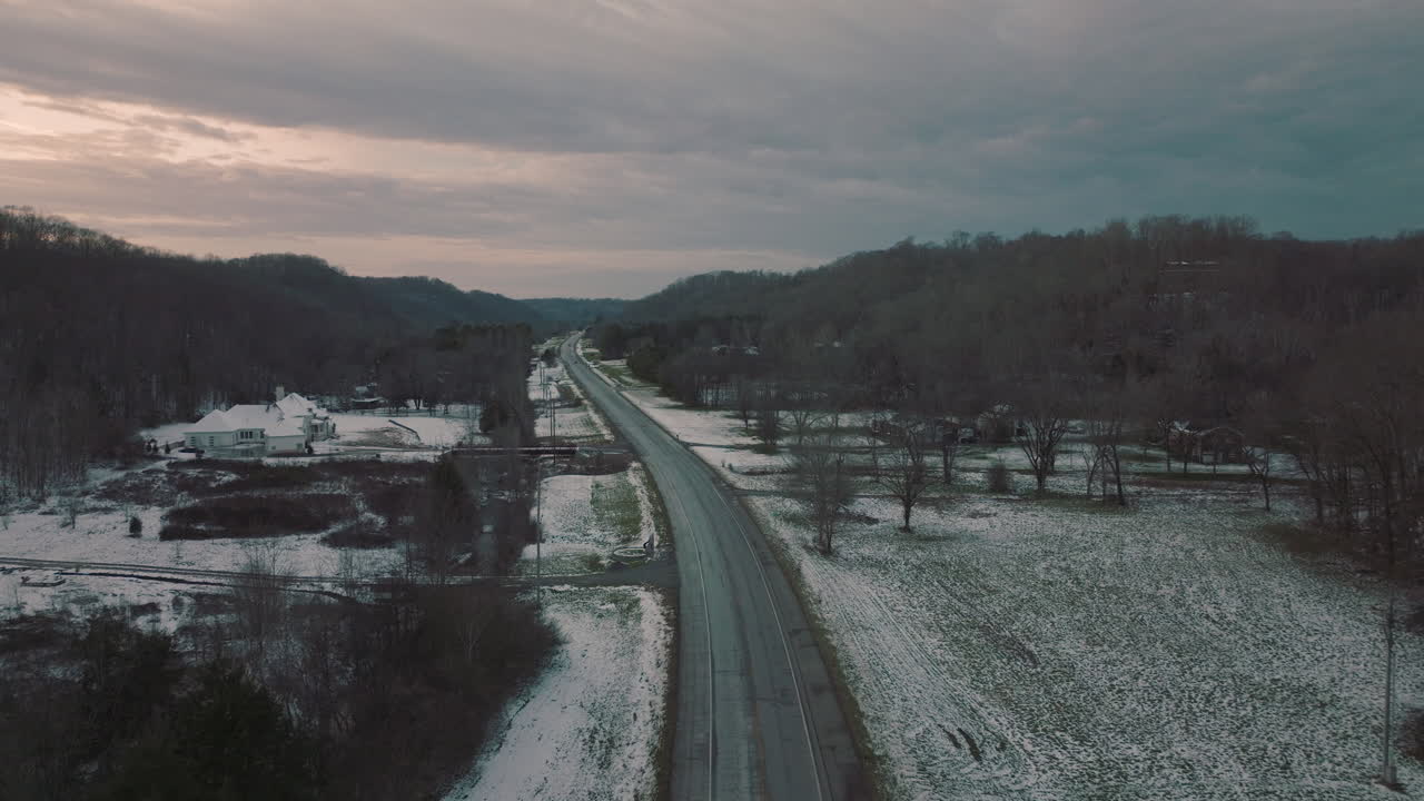 Flying along country road running under Natchez Trace Bridge at dusk in winter, landscape covered in light snow.