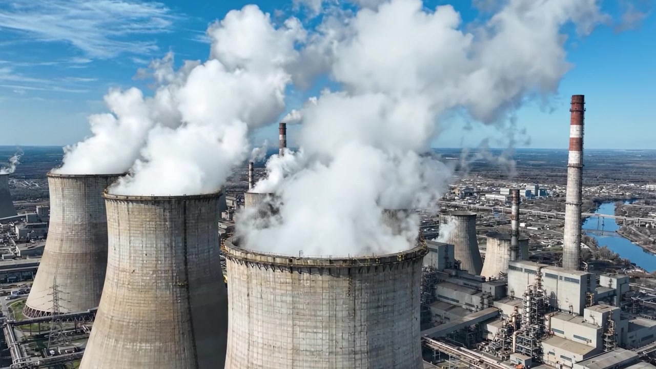 Grandi torri di raffreddamento industriali che emettono vapore sotto un cielo azzurro e limpido, mostrando la scala dell'infrastruttura di generazione di energia in un paesaggio urbano moderno
