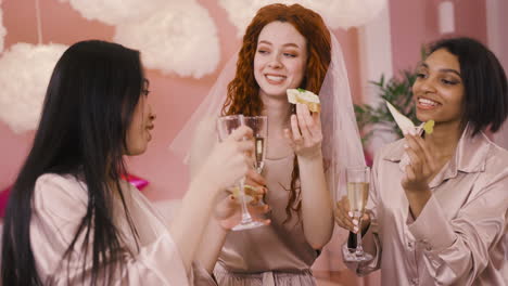 front view of three multiethnic friends toasting with crystal glasses of champagne and food celebrating bachelorette party