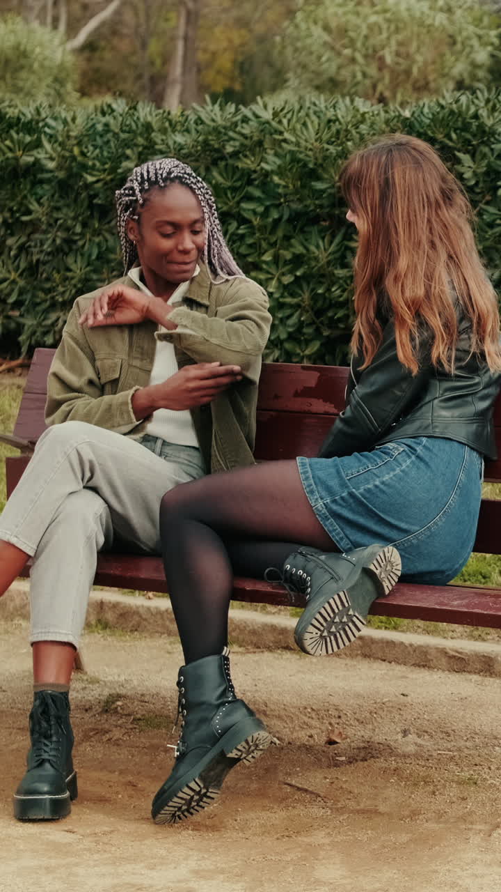 Two Young Women Talking and Gesturing on a Park Bench