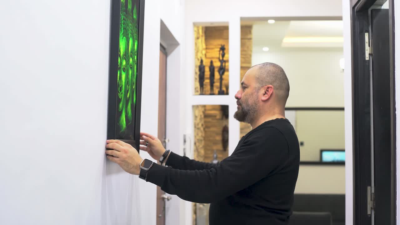 한 남자가 벽에 그림을 걸고 있습니다.