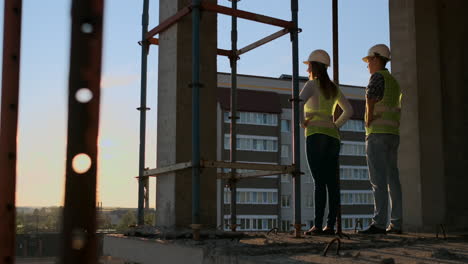 two chief engineer with a drawing in hand looking at the construction site. view from the back. chief engineer with blueprint in hand looking at the construction