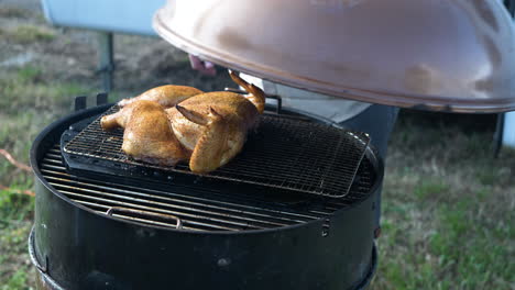 chicken being cooked on a bbq pit and the lid being placed over it