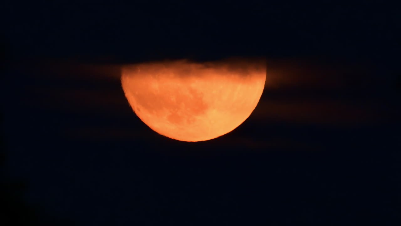 A stunning orange moon appears while drifting behind clouds in a night sky