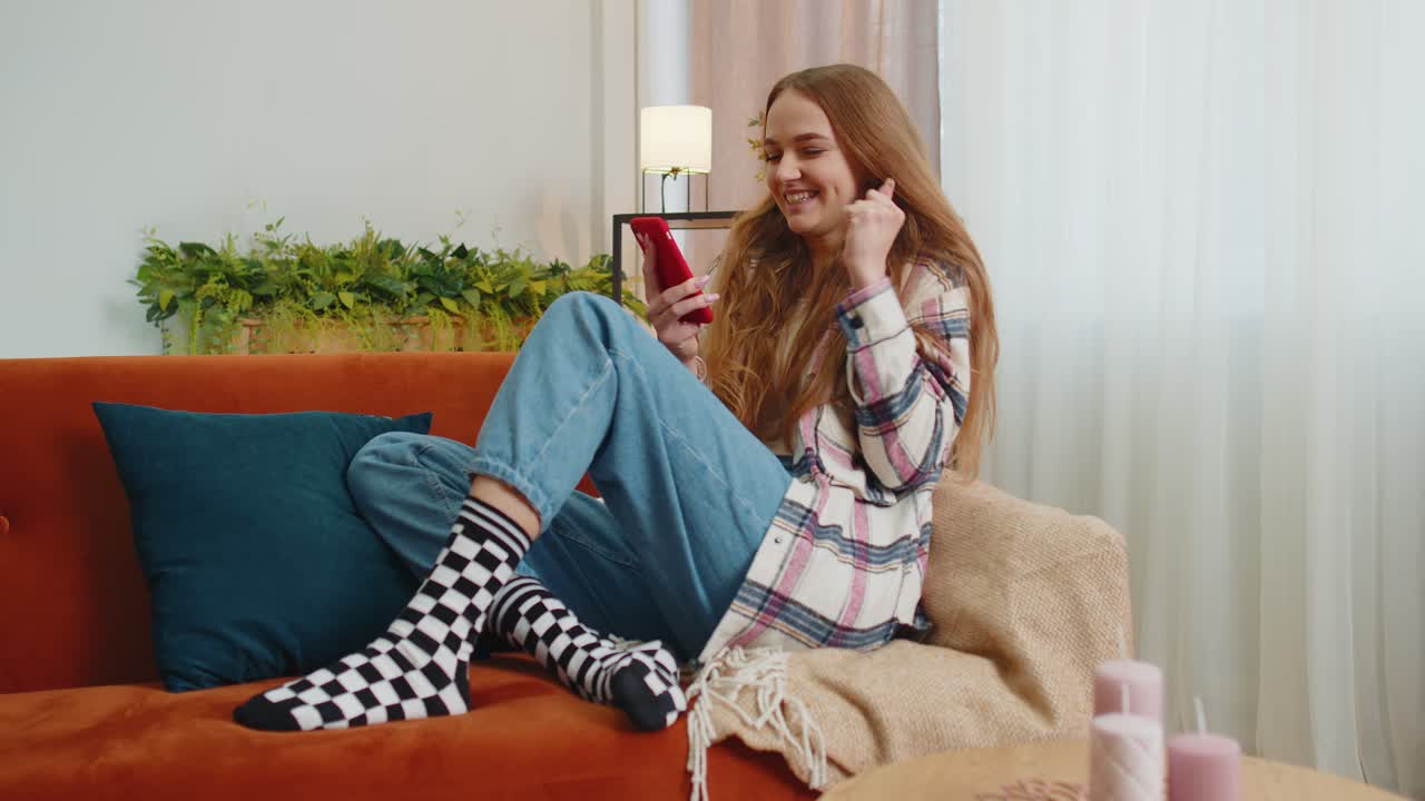 성인 젊은 여성은 집에서 휴대 전화를 사용하고, 타이핑하고, 브라우징하고, 와우, 네, 훌륭한 큰 승리를 발견했습니다.