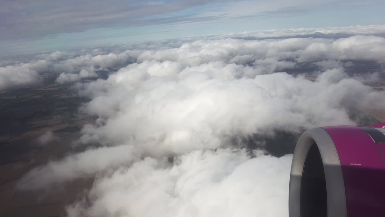 View of earth from a flying plane. Clouds, land with fields and villages, plane engine