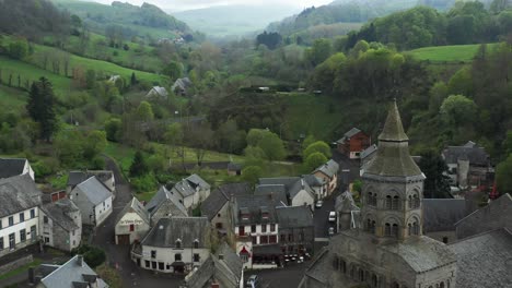 Breathtaking-misty-valley,-village-hamlet,-French-church-with-a-Gothic-feel