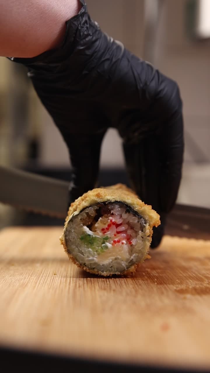 Kokki mustissa käsineissä leikkaamassa friteerattua sushirullaa