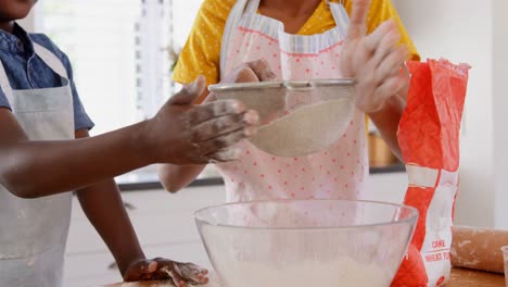 Vista-Frontal-De-Hermanos-Negros-Felices-Tamizando-Harina-En-La-Cocina-De-Una-Casa-Cómoda-4k