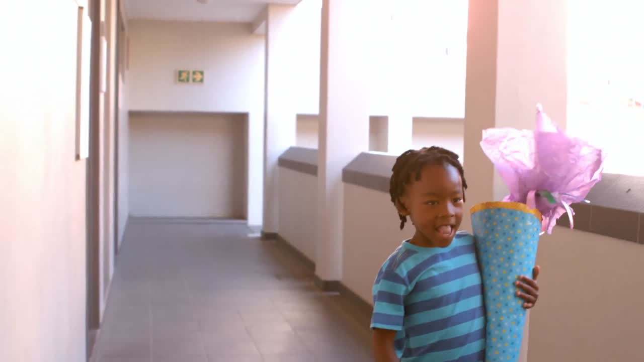 Cute schoolboy with gift running in corridor