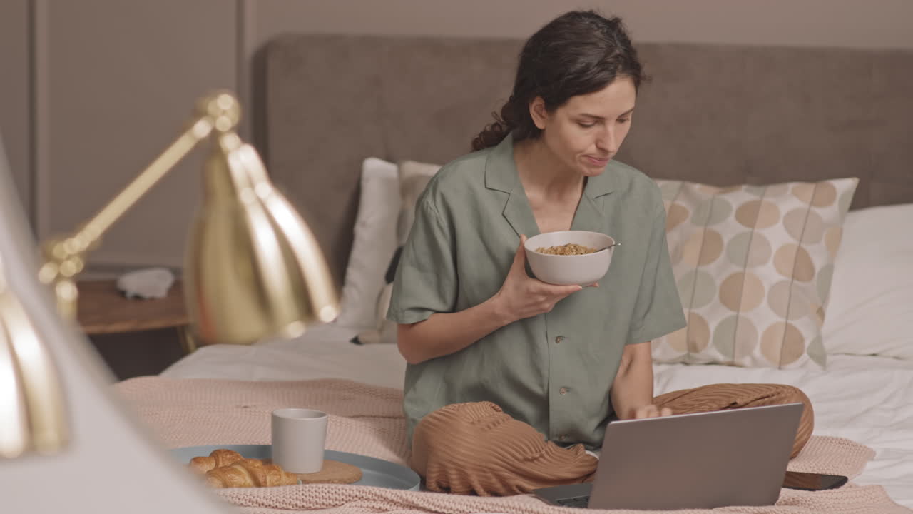 Woman Eating Breakfast and Using Laptop in Bed