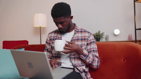 Young-man-using-laptop-computer-lying-on-sofa-at-home-working,-online-shopping-from-home-office