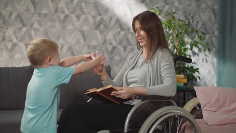 woman reads book while little boy bringing glass of water