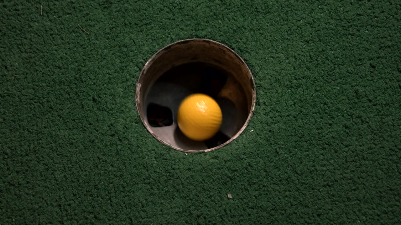una vista de pájaro de cerca de una mini pelota de golf amarilla cae en el hoyo de golf y rebota en el bolsillo en un campo