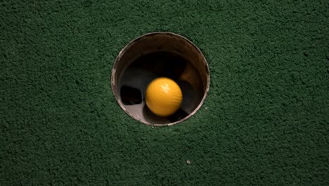 a close up birds eye view of a yellow mini golf ball falls into the golf hole and bounces in the pocket on a course