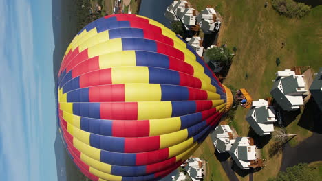 Vista-Aérea-Vertical-De-Coloridos-Globos-Aerostáticos-Volando-Sobre-El-Paisaje,-Disparo-De-Drones