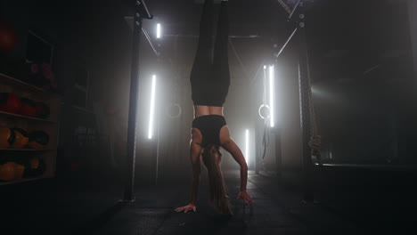 athletic woman is walking on hands in gym center training alone in fitness hall keeping fit