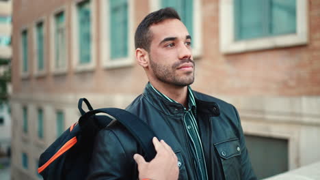 young man with backpack standing and smiling at camera outdoors.