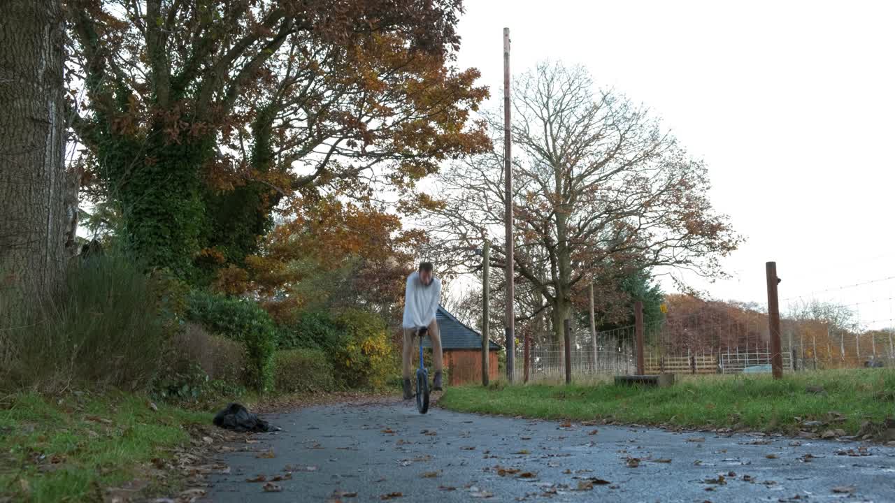 Young man performing unicycle tricks on an autumn road surrounded by trees