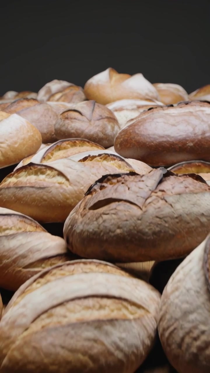 Vertical video: Pulling back camera revealing artisan loaves on oak board in studio showing scoring