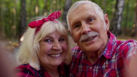 Senior-grandmother-grandfather-blogger-tourists-taking-selfie-photo-portrait-on-smartphone-in-forest