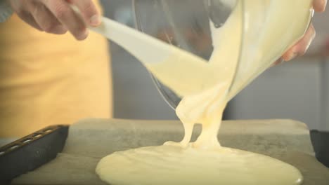 chef pours creamy biscuit dough from a glass bowl on a backing sheet on a plate