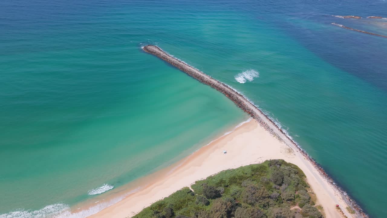 Drone establishing orbit of long breakwall stretching into turquoise sea off Blacksmiths Beach, NSW Australia