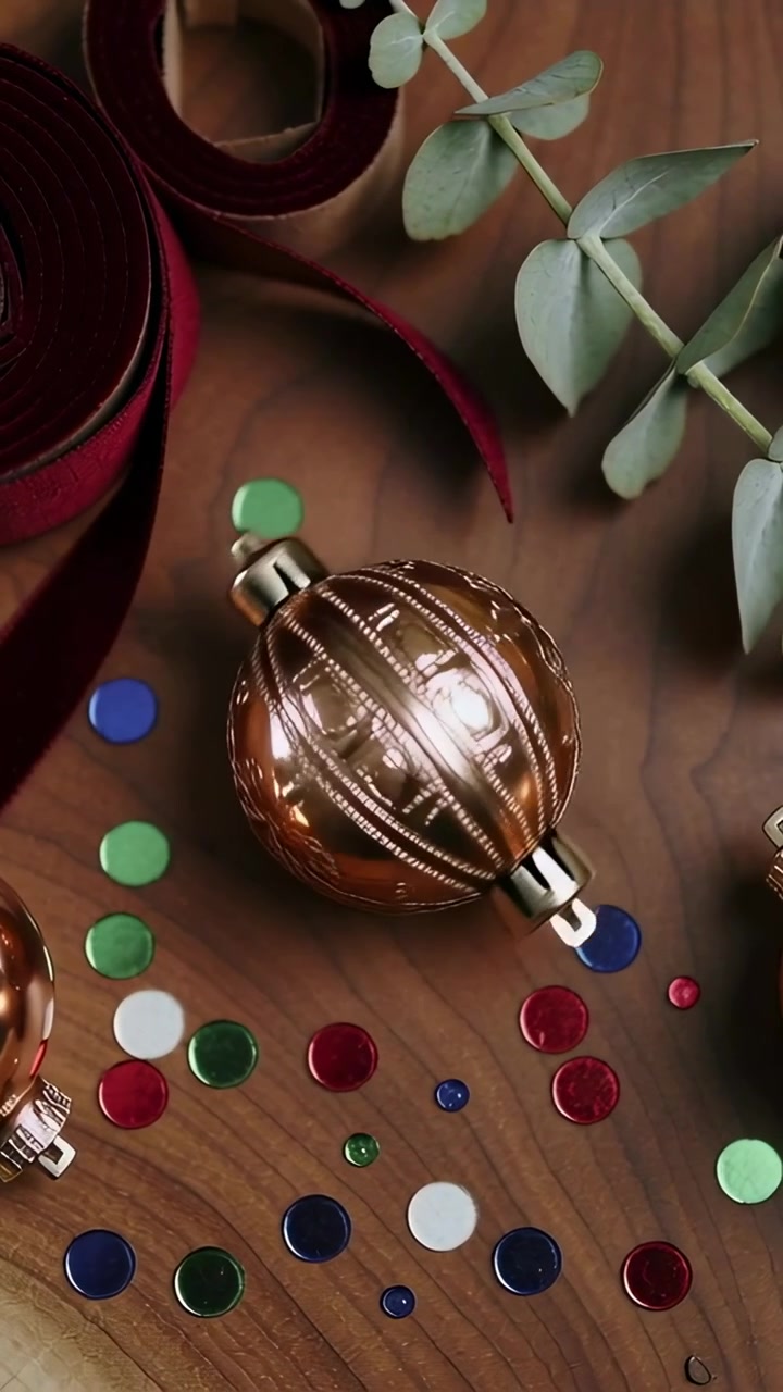 Vertical video: Camera filming copper ornament rotating on craft table, with ribbon and confetti