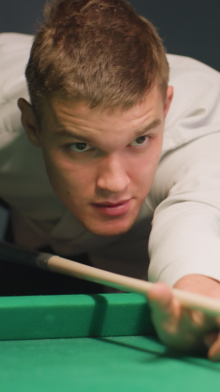 el jugador de camisa blanca se inclina sobre la mesa de billar verde, agarrando el palo de la bola con un enfoque intenso. los ojos bloqueados en la bola blanca mientras toma el tiro, demostrando precisión, concentración