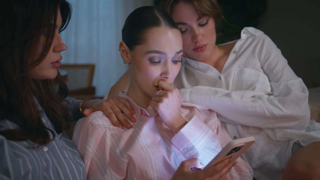 Girls sympathize female friend looking smartphone at evening home couch closeup