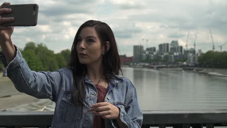 beautiful brunette latina tourist taking a selfie, posing while standing on the railing of a bridge in london