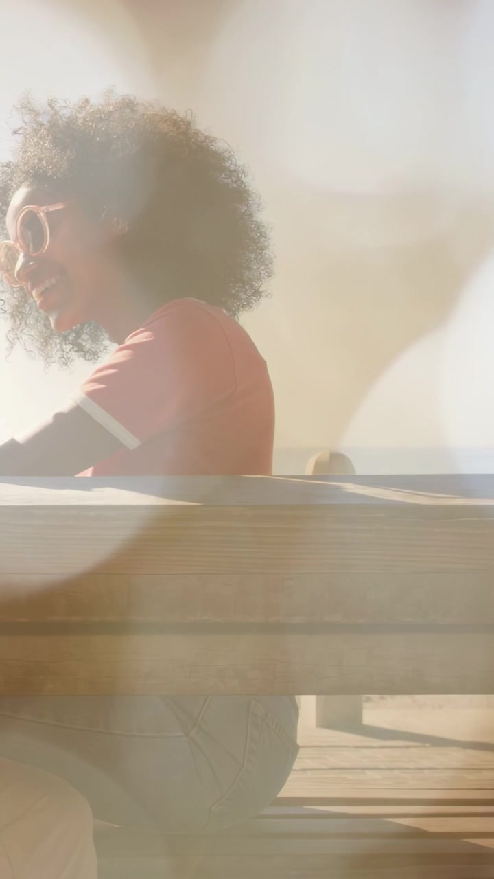 Vertical video: Woman on bench turning reacting to offscreen cue while sun flares add travel bokeh