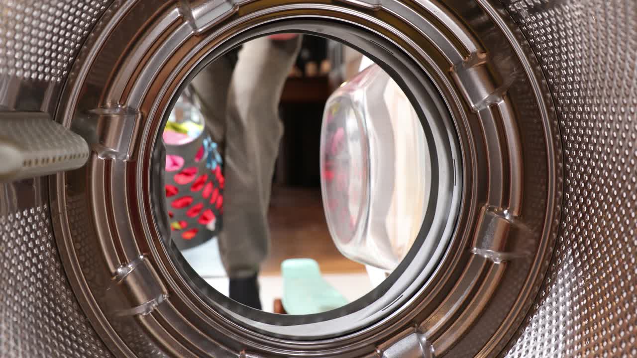 세탁기 드럼 안쪽의 전망. 젊은 남자가 세탁기에 세탁기를 고 있다. 내부의 전망