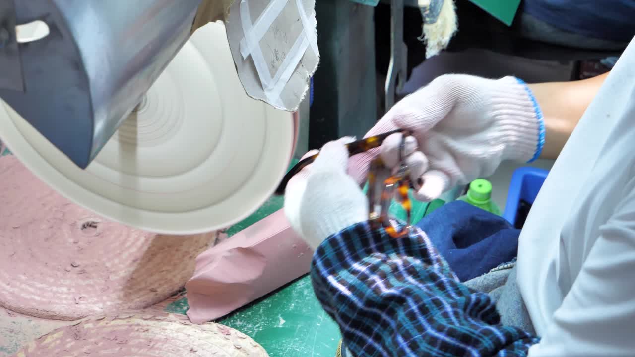 A worker uses a machine to polish the hinge of a glass frame in a spectacle factory. Captured in slow motion to showcase precision in craftsmanship. Danyang, Jiangsu Province, China.