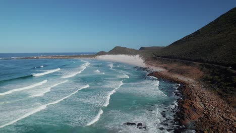 foamy ocean waves splashing on rocky shore of the beach in misty cliffs, cape town, south africa - drone shot