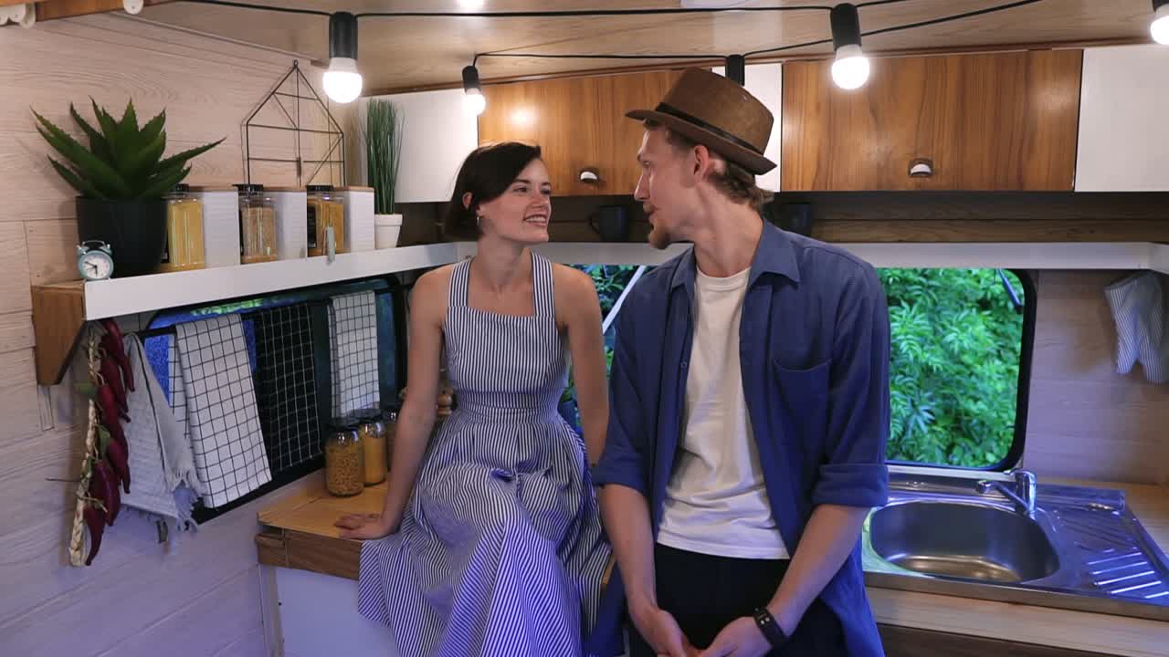 아름다운 커플이 밴의 세련된 부 ⁇ 에서 함께 시간을 보내고, 웃고, 포옹하고. 함께 즐기고, 휴가를 공유하고, 바 ⁇  집으로 여행하고. 드레스를 입은 여자가 부 ⁇  테이블에 앉아 있습니다.