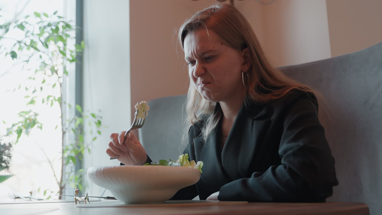 Dame reagiert schlecht auf Essen. Frau zeigt Missbilligung nach dem Probieren eines unappetitlichen Bissen zum Mittagessen. Dame verzieht das Gesicht und äußert Unzufriedenheit beim Probieren eines unappetitlichen Salats während ihrer Arbeitspause.