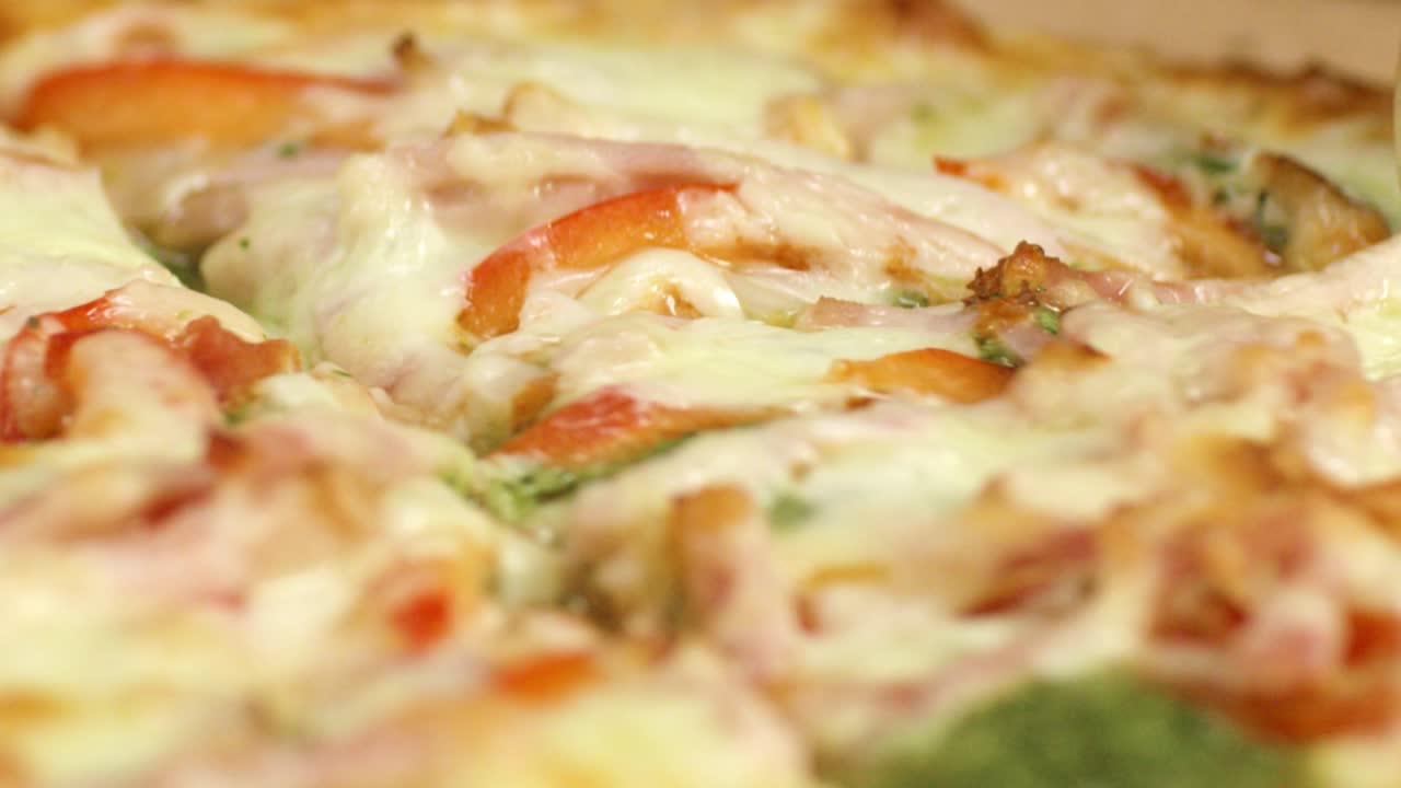 Close-up of a sliced pizza with ham, tomatoes, and basil
